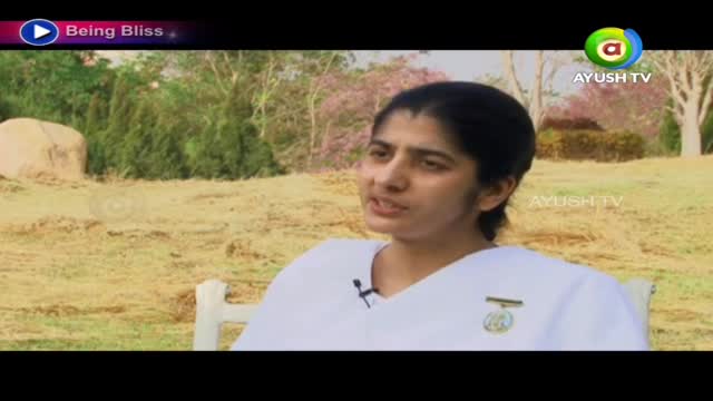 A woman in a white shirt speaks, a small microphone clipped to her collar. The scene is outdoors, with the Ayush TV logo visible in the corner.
