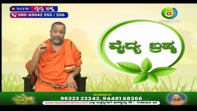 A man in an orange robe gestures with his hand as he speaks, likely on a program from Ayush TV in India. The backdrop includes a logo and text in a local language.
