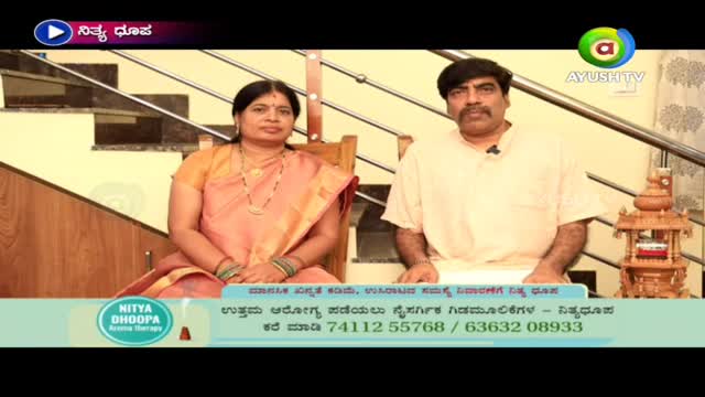 A man and woman sit side-by-side, facing the camera in a set decorated with stairs and a small wooden display. The Ayush TV logo sits in the top right corner, and a graphic with a phone number is at the bottom.
