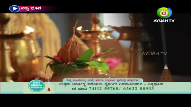 A coconut sits atop a brass pot, adorned with green leaves and red flowers. The scene is lit by several lamps, and the Ayush TV logo is visible.
