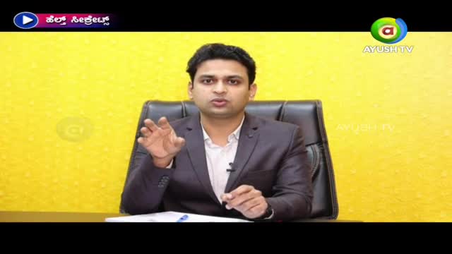 A man in a suit gestures with his hands, speaking directly into the camera. The Ayush TV logo is visible in the corner, and the background is a solid yellow.
