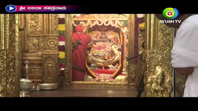 A person in a red robe is tending to a golden shrine, visible on Ayush TV. The intricate carvings and decorations gleam under the lights.
