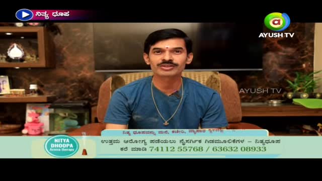 A man in a blue shirt is seated, speaking directly to the camera. The Ayush TV logo is visible in the top right corner, and a graphic at the bottom advertises "Nitya Dhoopa Aroma Therapy."
