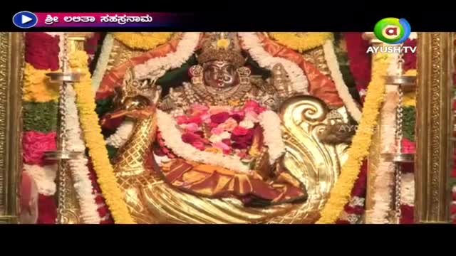 A gilded deity sits on a peacock throne, surrounded by garlands of flowers. Ayush TV is broadcasting from what appears to be a temple in India, with a title card in the corner.
