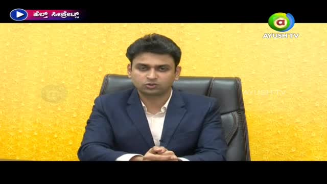 A man in a blue suit sits in a black chair, speaking directly to the camera against a yellow background. The Ayush TV logo is visible in the corner.
