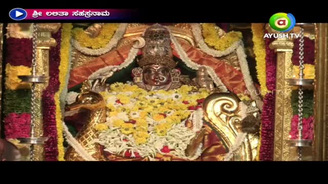 A decorated deity sits at the center, framed by colorful garlands and ornate gold fixtures. The Ayush TV logo is visible in the corner, suggesting this is a broadcast from India.
