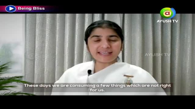 A woman in white is speaking, a small microphone clipped to her collar. The Ayush TV logo is visible, along with text at the bottom of the screen.
