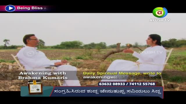 Two people in white robes sit in chairs outdoors, facing each other. A segment from Ayush TV, "Awakening with Brahma Kumaris," is being filmed in a field.
