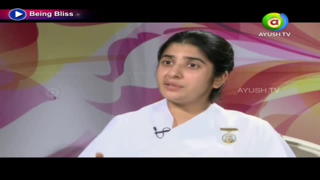 A woman in a white outfit speaks directly to the camera, a small microphone clipped to her collar. The Ayush TV logo is visible in the corner, and the backdrop is a soft, colorful pattern.

