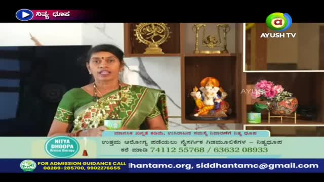 A woman in a green sari is speaking, holding a cup, with a backdrop of religious statues and a shelf. The Ayush TV logo is visible in the top right corner.
