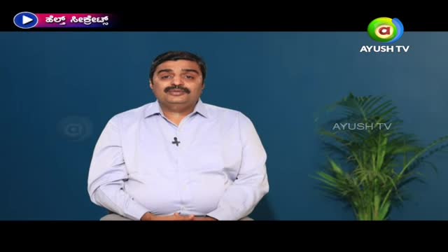 A man in a light blue shirt sits in front of a dark blue backdrop, speaking into a small microphone. The Ayush TV logo is visible in the corner.
