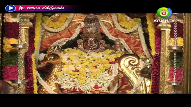 A deity, adorned with a jeweled crown, is the focal point, surrounded by garlands of yellow and white flowers. The broadcast, marked by Ayush TV, appears to be from India, with the words in the upper left corner.
