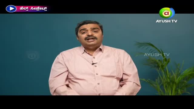 A man in a pink shirt speaks directly to the camera, likely on Ayush TV in India. Behind him, a plant sits to the right, and the Ayush TV logo is visible.
