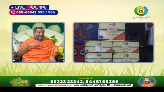 On Ayush TV, a man in an orange robe gestures while sitting in front of a backdrop. Several boxes of products are stacked nearby.
