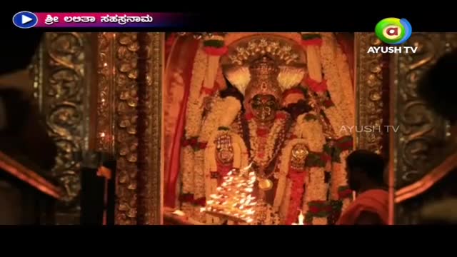 A golden idol, adorned with garlands, is the focal point of a temple shrine, lit by a small, brass lamp. Ayush TV's logo is visible, indicating a broadcast from India.
