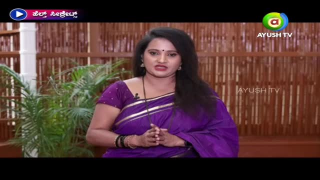 A woman in a purple sari is speaking directly to the camera on Ayush TV. The background is a bamboo-style wall, and the logo for "Ayush TV" is visible.
