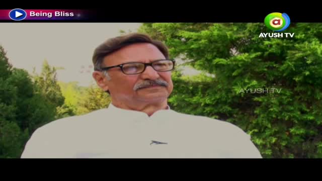 A man in glasses and a white shirt is speaking, possibly for Ayush TV. Behind him, lush green foliage fills the background.
