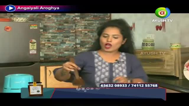 A woman is holding a wooden spoon, gesturing as she speaks on what appears to be an Ayush TV cooking show. The backdrop is a kitchen, and a small jar of something sits on the counter.
A woman is holding a wooden spoon, gesturing as she speaks on what appears to be an Ayush TV cooking show. The backdrop is a kitchen, and a small jar of something sits on the counter.