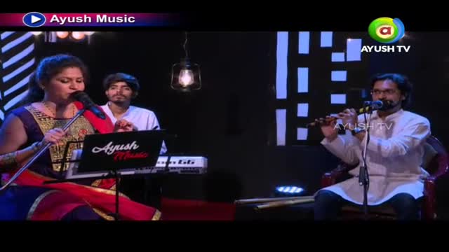 The woman in a colorful sari sings into a microphone, while a man plays the flute across the stage. Behind her, another man accompanies on a keyboard, all under the Ayush Music banner.
The woman in a colorful sari sings into a microphone, while a man plays the flute across the stage. Behind her, another man accompanies on a keyboard, all under the Ayush Music banner.