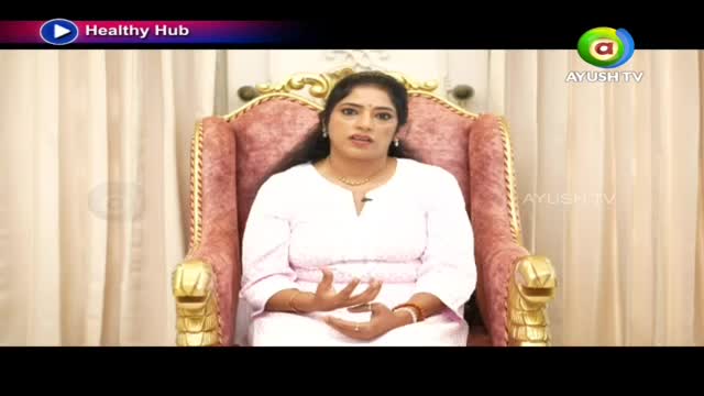 A woman in a white outfit sits in a plush, ornate chair, her hands gesturing as she speaks. The Ayush TV logo appears on screen, indicating a broadcast from India.