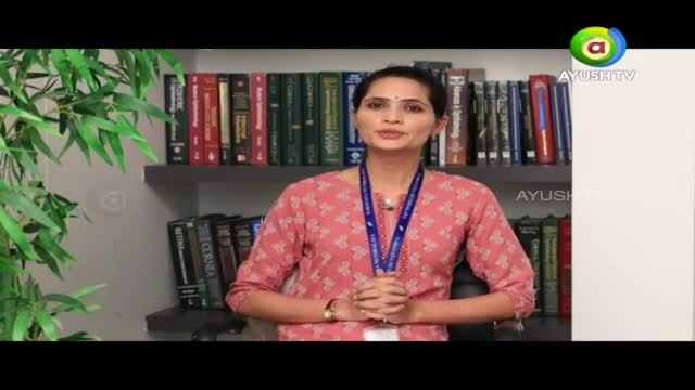 A woman in a pink patterned kurta stands before shelves of books. She wears a blue lanyard with an ID card.