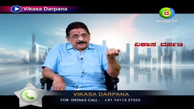 A man with a mustache and glasses gestures with his right hand while speaking. He wears a light blue collared shirt and sits in a dark chair.