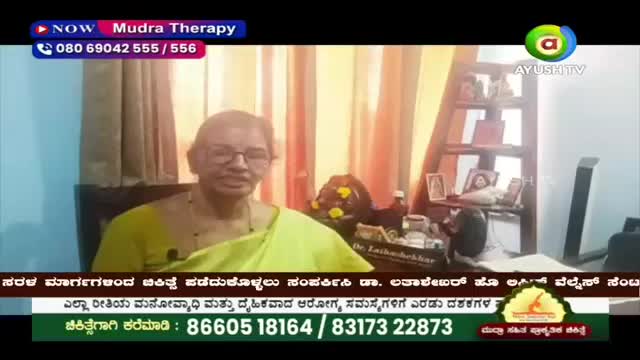 A woman in a bright yellow sari speaks directly to the camera. A graphic at the top of the screen announces "NOW Mudra Therapy" and displays a phone number.