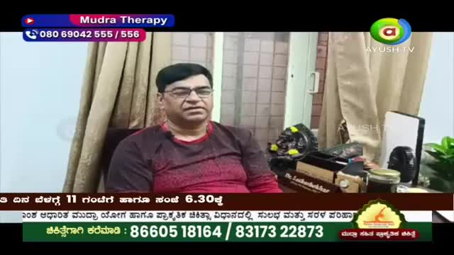 A man with glasses sits in front of a tan curtain, a maroon shirt on. On a table beside him, a jar of honey and some medical equipment rest. A man with glasses sits in front of a tan curtain, a maroon shirt on. On a table beside him, a jar of honey and some medical equipment rest.