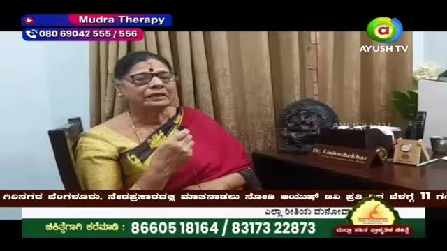 A woman in a red and gold sari speaks, her hand gesturing as she explains something. On the desk behind her, a nameplate reads "Dr. Latha Shekhar." A woman in a red and gold sari speaks, her hand gesturing as she explains something. On the desk behind her, a nameplate reads "Dr. Latha Shekhar."