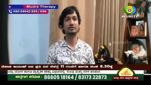 A man in a patterned shirt speaks directly to the camera, with a shelf of books and a small statue behind him. A graphic overlay indicates "Mudra Therapy" and a phone number. A man in a patterned shirt speaks directly to the camera, with a shelf of books and a small statue behind him. A graphic overlay indicates "Mudra Therapy" and a phone number.