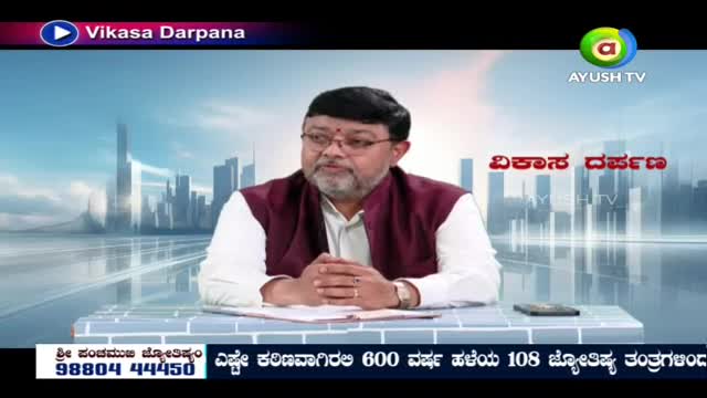 A man with glasses and a beard sits at a desk, his hands clasped. He wears a white shirt and a maroon vest, speaking into a microphone on a television program. A man with glasses and a beard sits at a desk, his hands clasped. He wears a white shirt and a maroon vest, speaking into a microphone on a television program.
