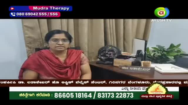 A woman in a maroon shawl sits behind a desk, looking directly ahead. On the desk, a nameplate reads "Dr. Lavanya Kumar."