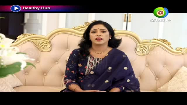 A woman in a dark blue salwar kameez speaks animatedly from a plush, tufted sofa. The Ayush TV logo appears in the corner, indicating this broadcast originates from India.