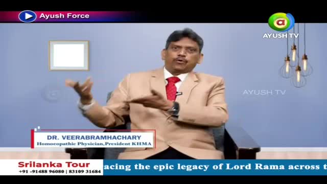 A man in a tan suit and red tie gestures with his hands while speaking. The Ayush TV logo appears on screen.