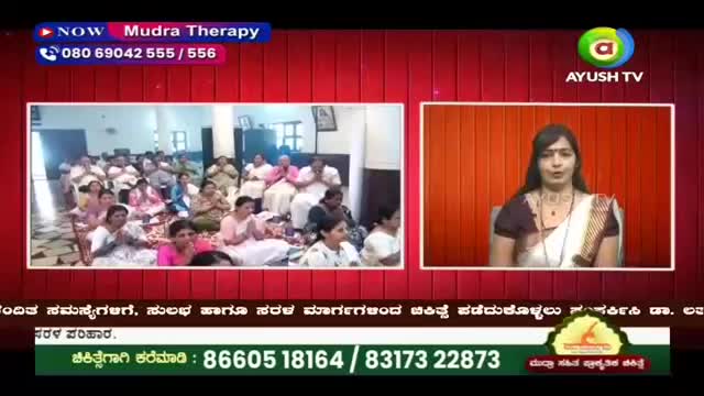 A large group of people sits on the floor, many with their hands pressed together in prayer. On the right, a woman in a sari speaks directly to the camera.