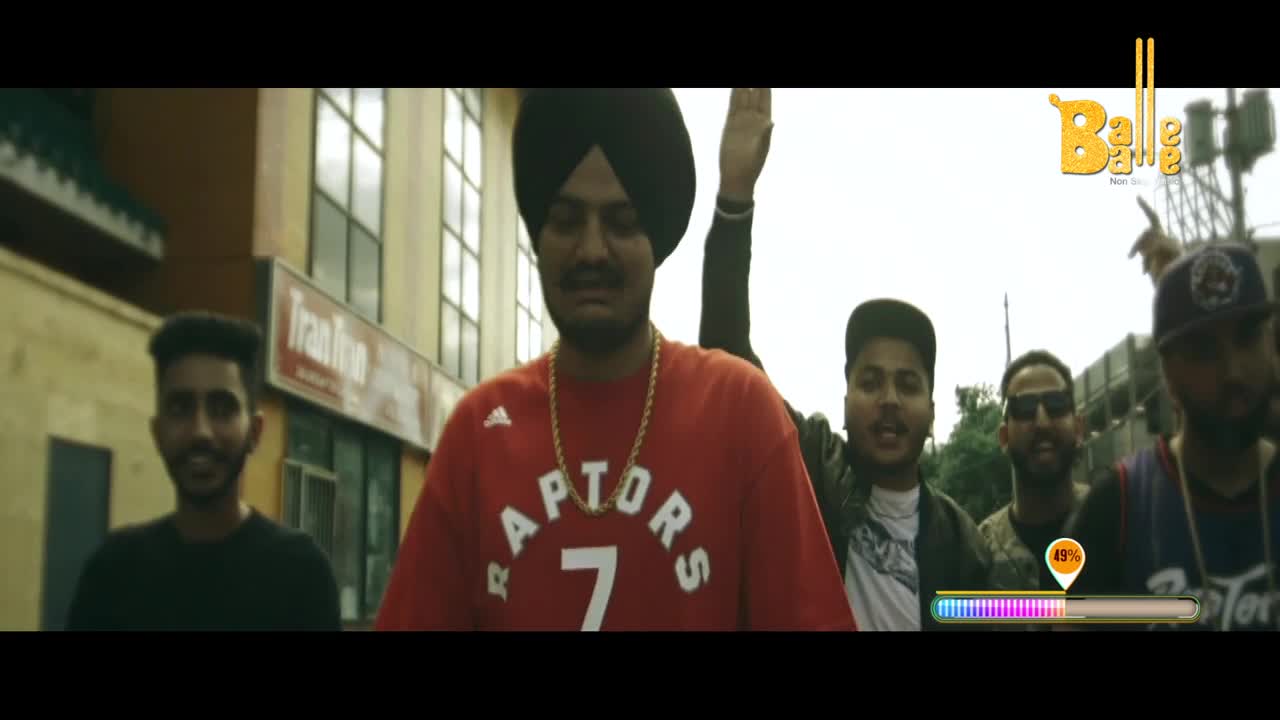 A man in a red Raptors shirt and gold chain stands front and center, surrounded by a group of guys, some with arms raised. The Balle Balle logo sits in the corner, and a progress bar at the bottom shows the video's progress.

