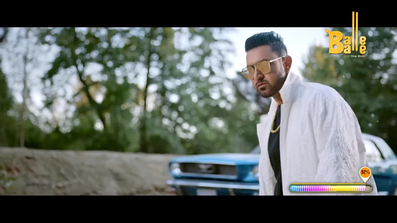 A man in a white jacket and sunglasses stands in front of a classic blue car, looking directly at the camera. The Balle Balle logo is in the top right corner, and a progress bar at the bottom shows the song's progress.
