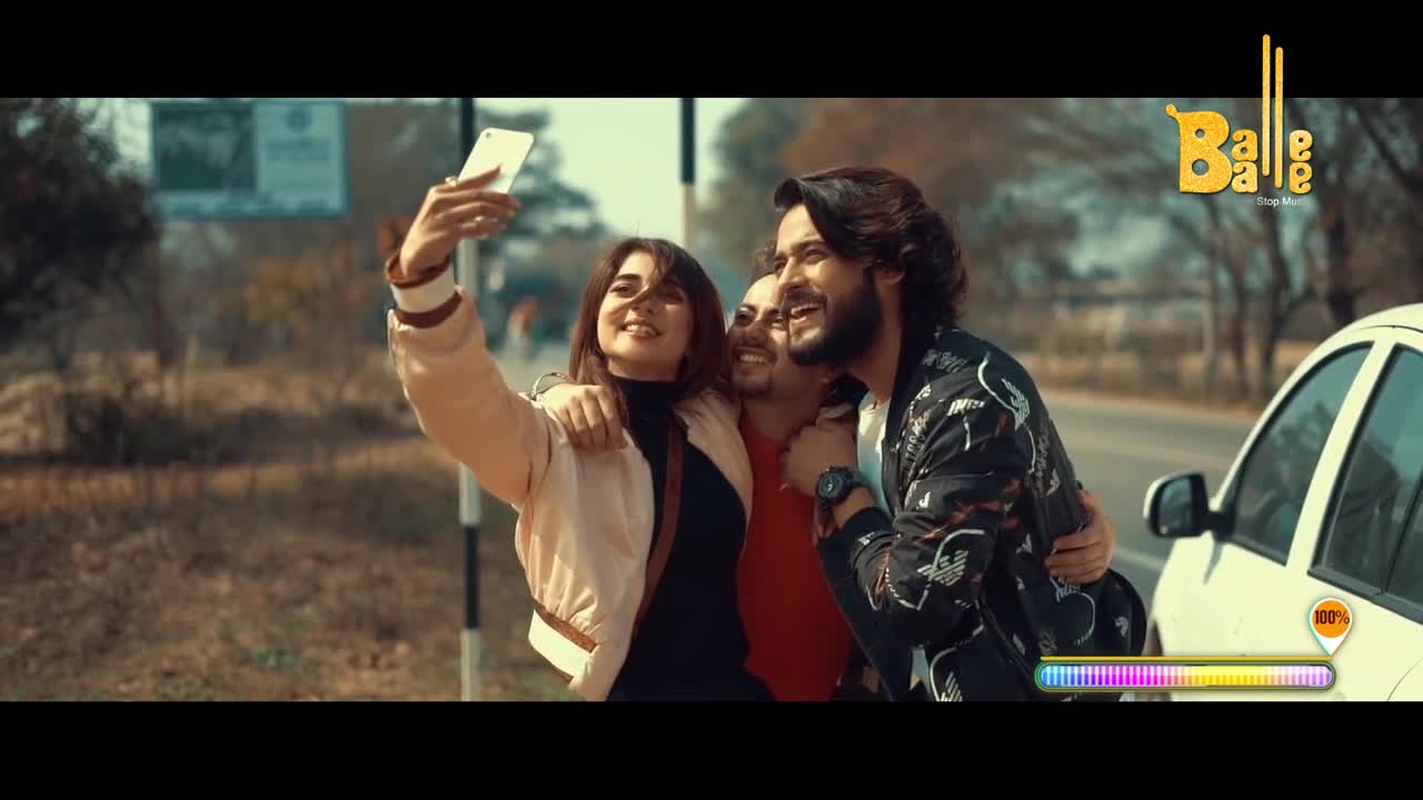 A woman with a phone in hand is taking a selfie with two smiling men, all of them close together. A white car is parked nearby, and the "Balle Balle" logo is visible in the corner.
