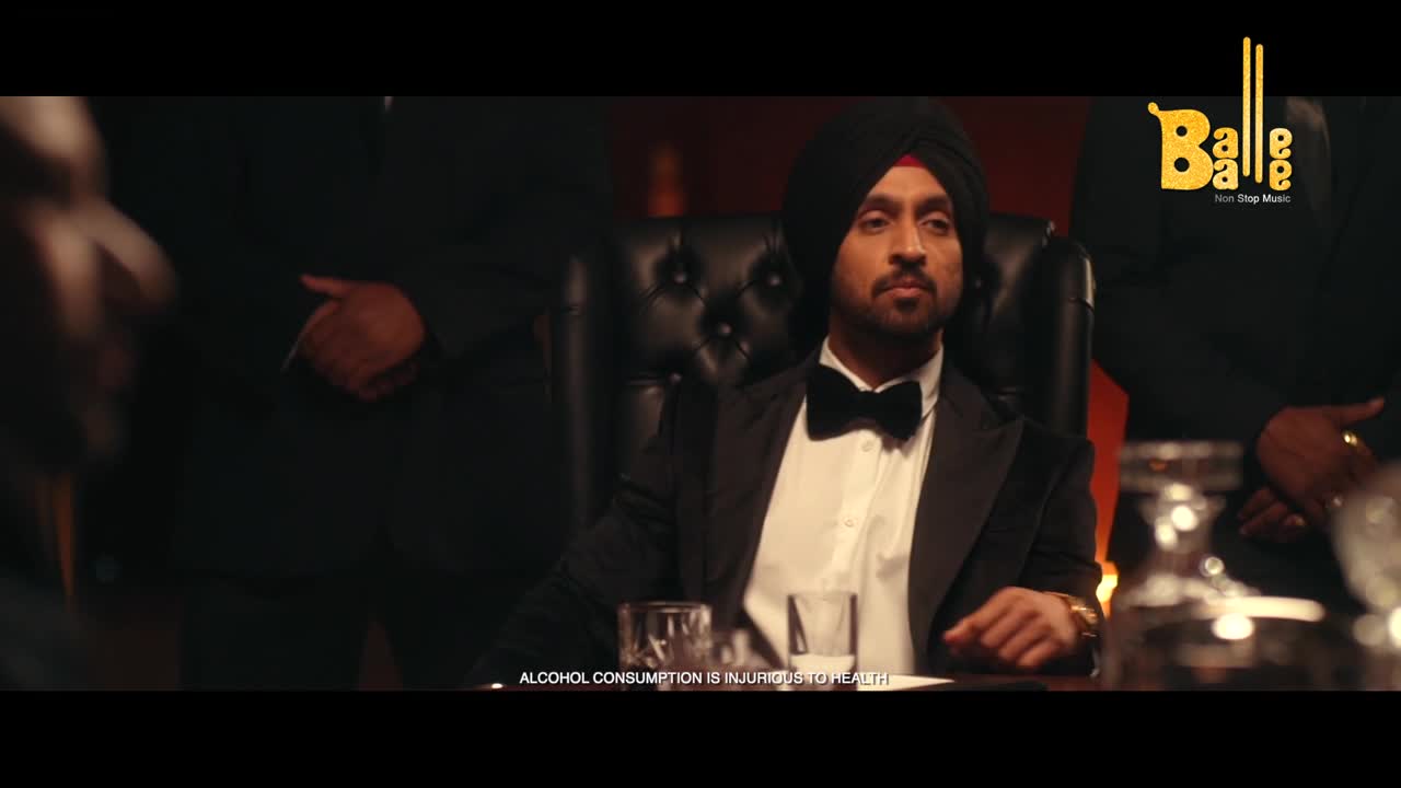 A man in a turban and bow tie sits at a table, flanked by other men in suits. The "Balle Balle" logo is visible in the corner, and a warning about alcohol is at the bottom.
