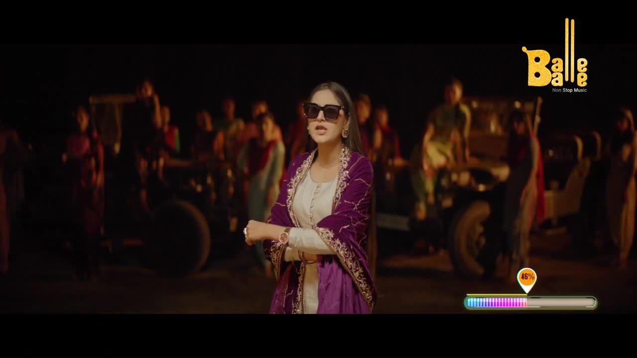 A woman in sunglasses and a purple shawl gestures toward the camera, a crowd of people and a tractor are behind her. The "Balle Balle" logo sits in the corner, and a progress bar ticks along at the bottom.
