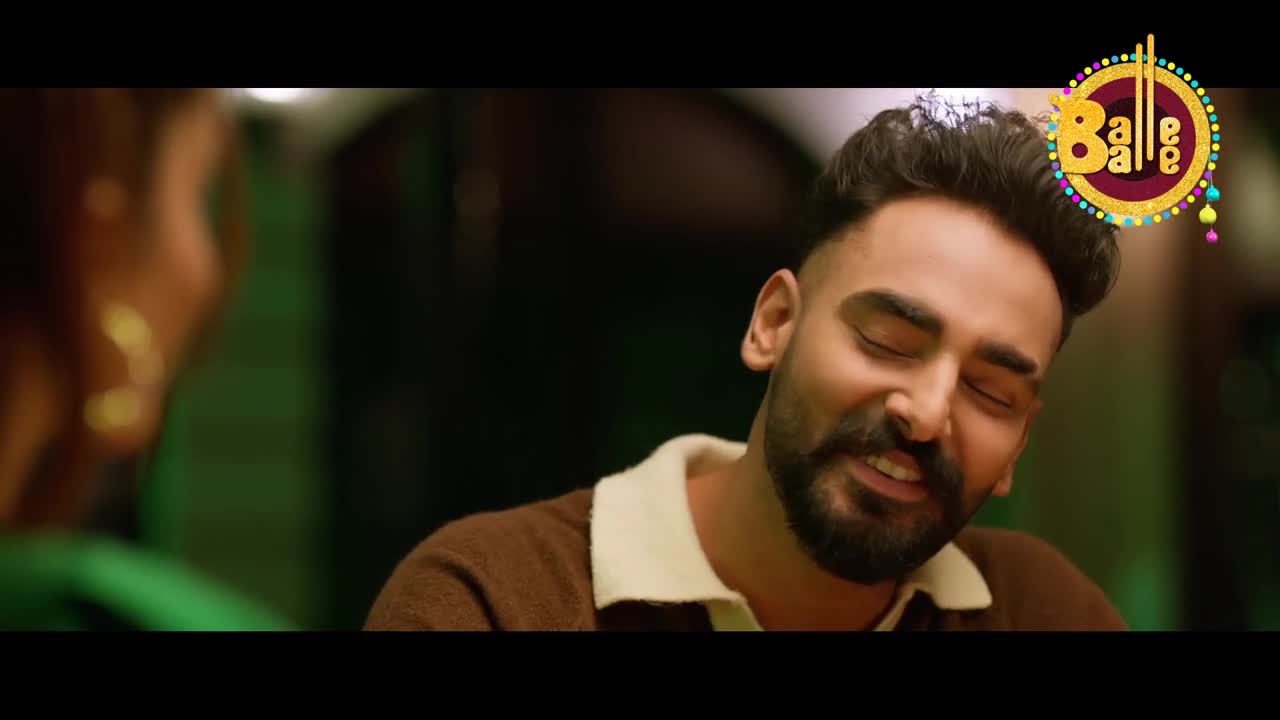 A man with a neatly trimmed beard and a brown sweater smiles, eyes closed, as if listening intently. The "Balle Balle" logo sits in the corner, a colourful emblem of the music video's origins.
