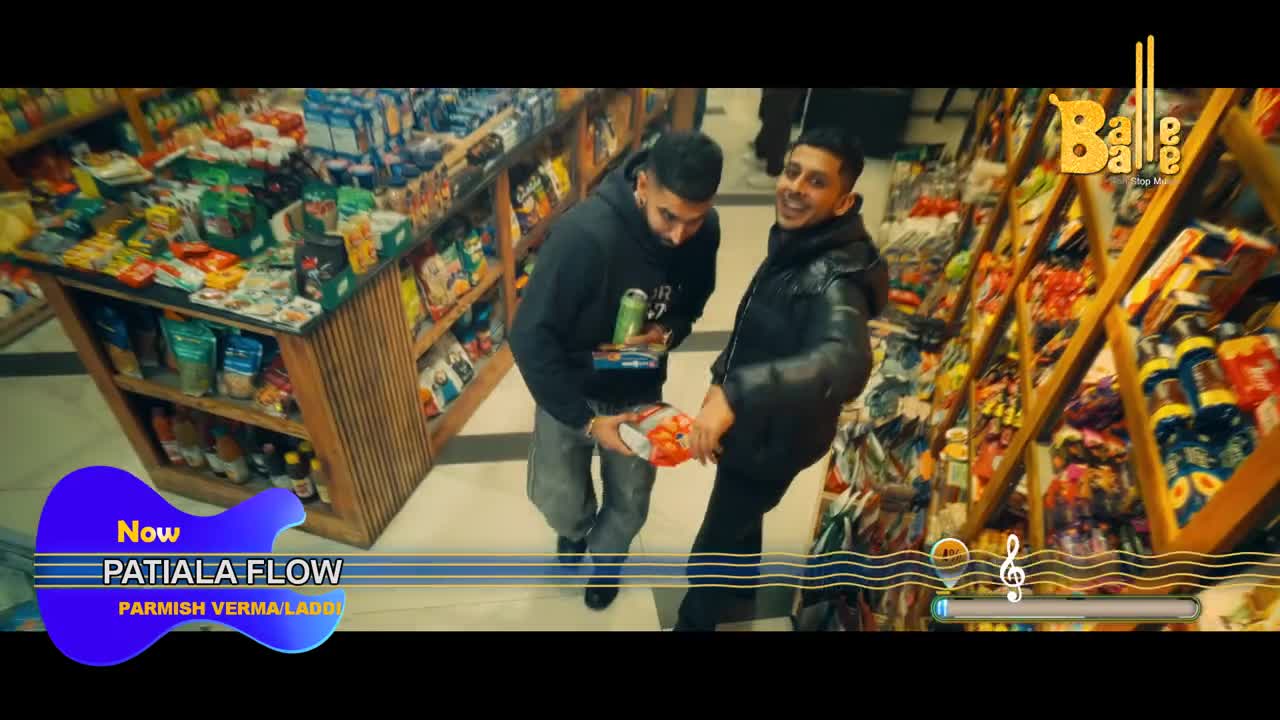Two men are in a shop, one holding a bag of chips and the other smiling. The scene is from a music video, as indicated by the "Balle Balle" logo and the song title overlay.

