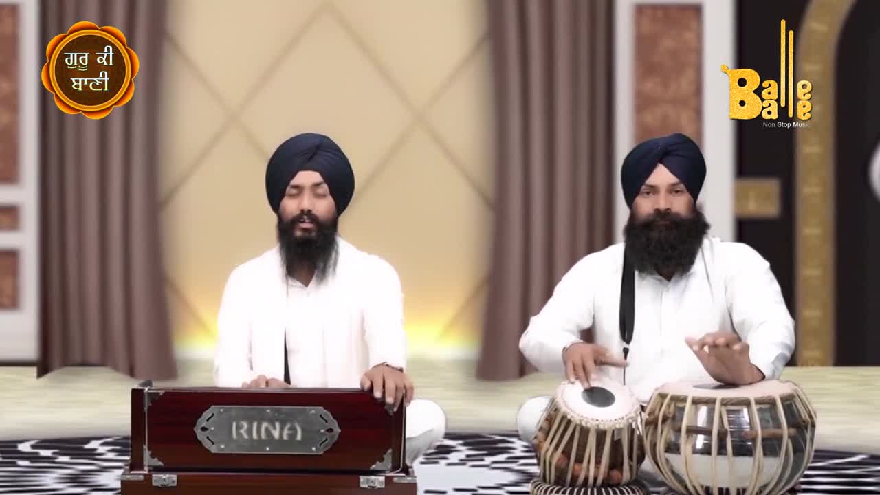 Two men in white are seated, one playing a harmonium and the other a tabla. The musician on the right keeps a steady rhythm with his hands.
