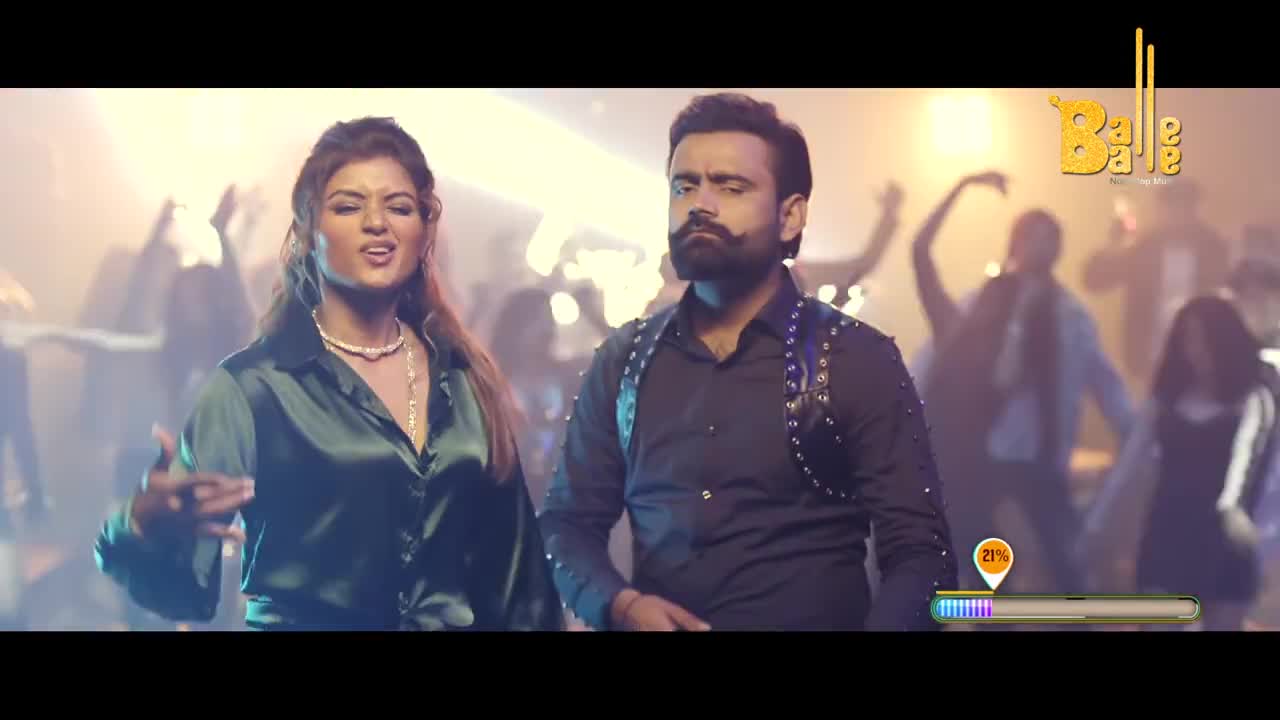 The woman in the green shirt gestures with her hands as she sings, while the man beside her stares forward. Behind them, a crowd of people dance in the hazy light, the Balle Balle logo visible in the corner.
