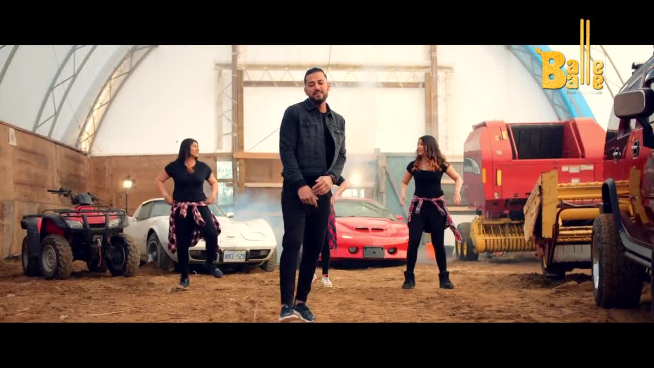 A man in a black jacket stands center stage, while three women in black outfits dance around him in front of cars and farm equipment. The "Balle Balle" logo sits in the top right corner of the frame.
