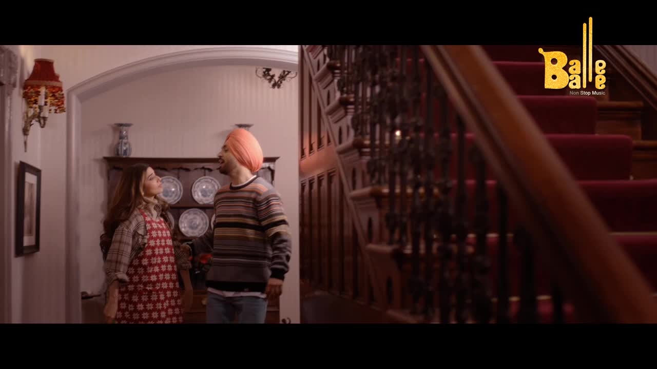 A man in a turban and striped sweater stands with a woman wearing an apron in a hallway, looking up at the staircase. The Balle Balle logo sits in the top right corner.
