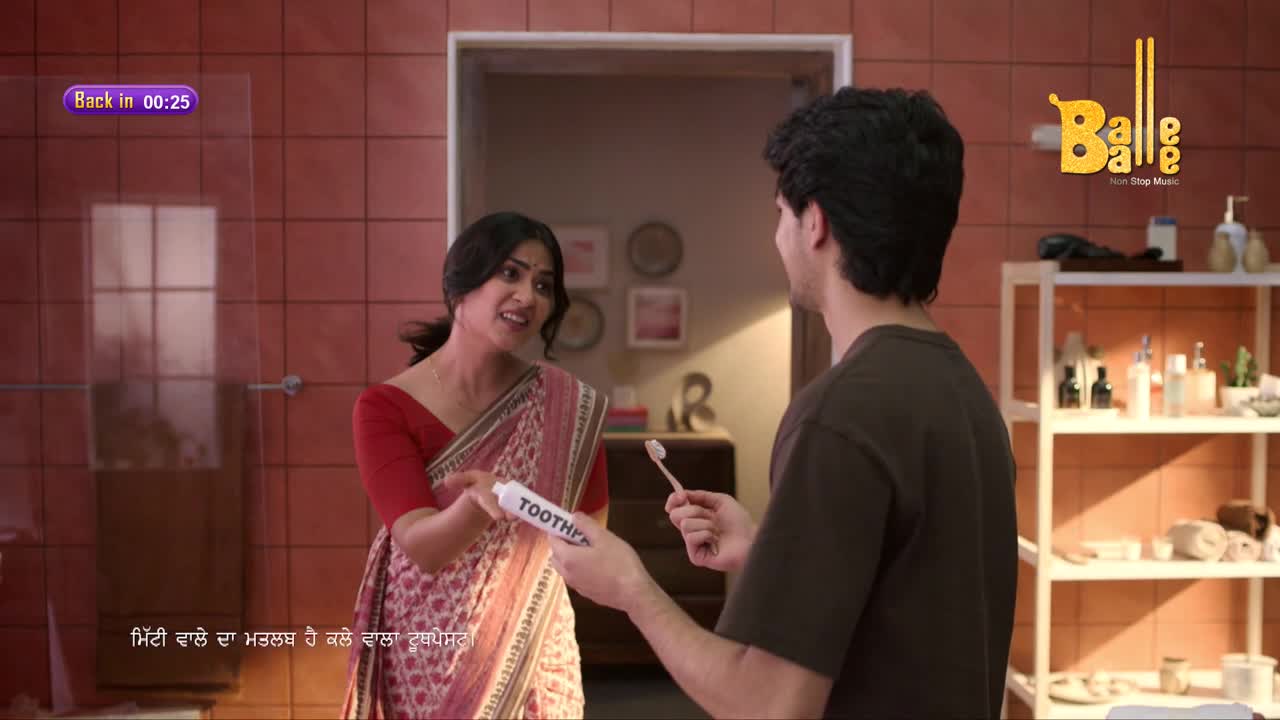 A woman in a saree gestures emphatically, offering a tube of toothpaste to a young man holding a toothbrush. The scene unfolds in a bathroom, with the "Balle Balle" logo visible in the corner.
