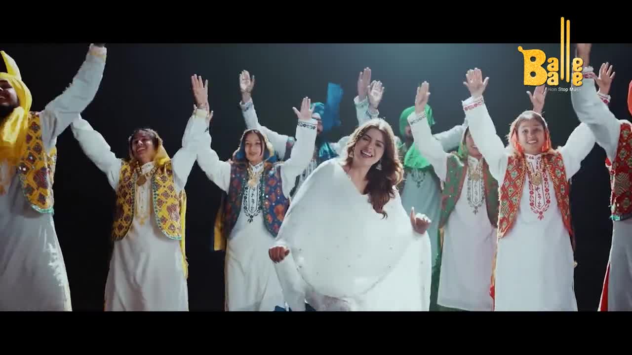 A group of people in traditional Indian clothing are dancing, arms raised in the air. The woman in the center, draped in white, smiles broadly as she moves to the music.
