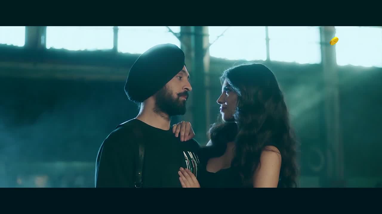 A man in a black turban gazes at a woman, his hand resting gently on her shoulder. Their faces are close, illuminated by a cool, blue-green light.
