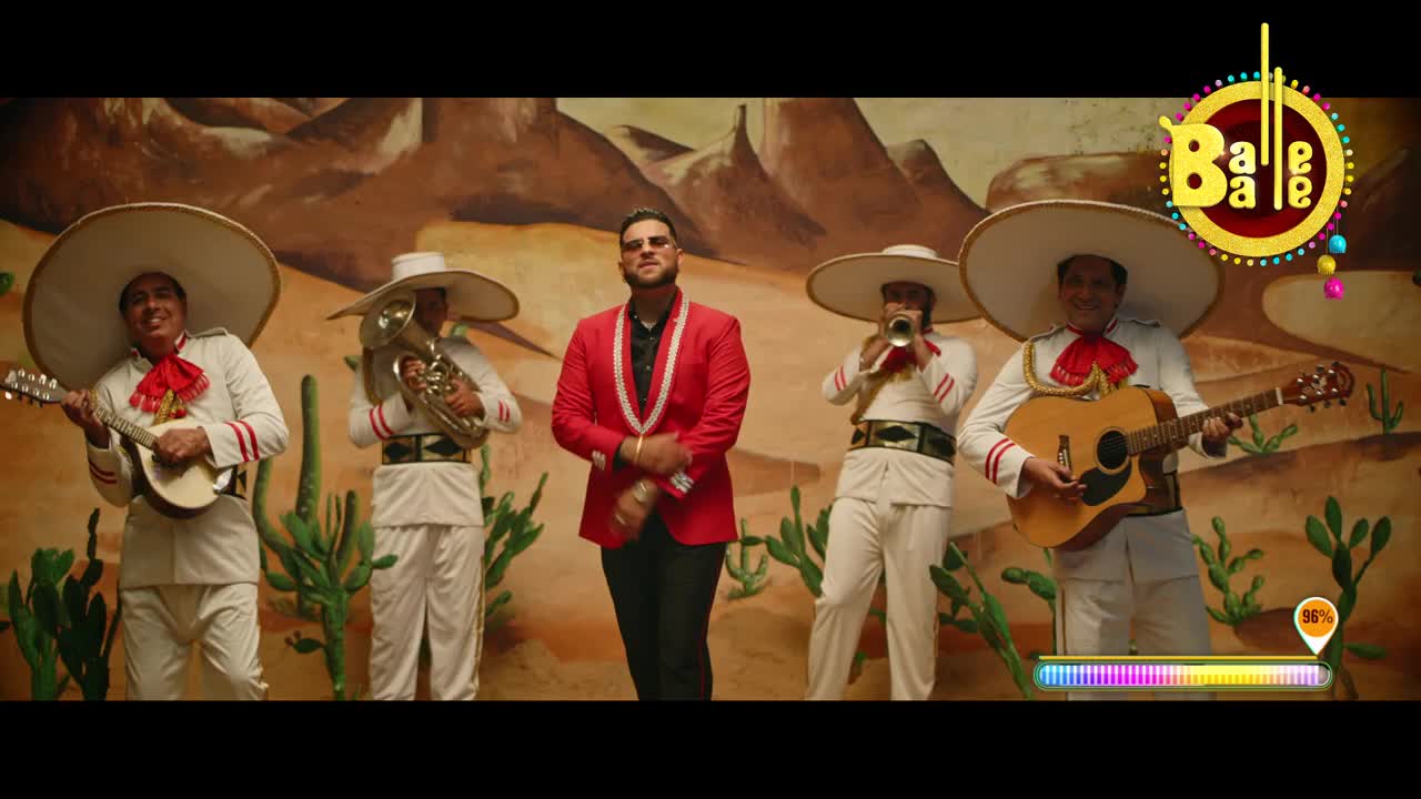 A man in a red jacket stands center stage, flanked by musicians in white suits and sombreros. The band plays, the music's energy matching the Balle Balle logo at the top right.

